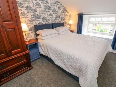 A bedroom with a bed white bedspread blue headboard two bedside tables with lamps wooden wardrobe and window with blue curtains at The Old Post Office in Praze-An-Beeble