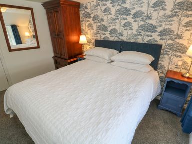 A bedroom with a bed with white bedding blue headboard wooden wardrobe and two blue bedside tables with lamps at The Old Post Office in Praze-An-Beeble