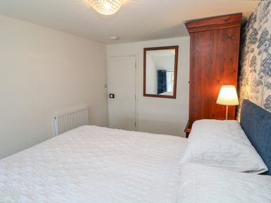 A bedroom with a bed white bedding a wooden wardrobe a lamp and a mirror on the wall at The Old Post Office in Praze-An-Beeble