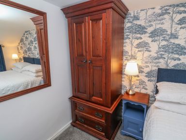 A bedroom corner with a wooden wardrobe a blue bedside table with a lamp and a bed with white bedding at The Old Post Office in Praze-An-Beeble