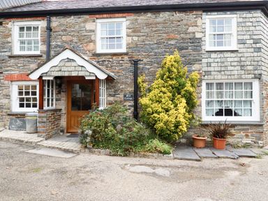 Stone cottage exterior with wooden door bushes and potted plants at Mill Cottage in St Neot