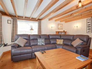 A living room with a large leather sectional sofa and wooden coffee table at Mill Cottage in St Neot