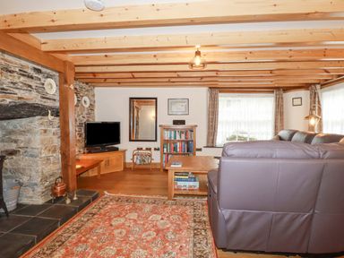 A living room with exposed wooden beams stone fireplace and leather sofa at Mill Cottage in St Neot