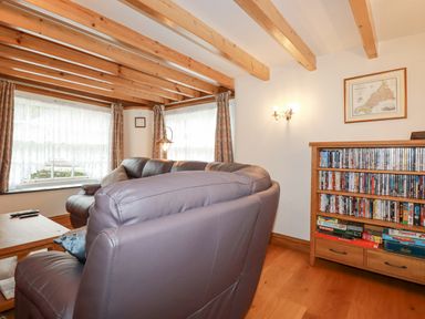 A living room with leather sofas wooden beams and a bookshelf with DVDs and board games at Mill Cottage in St Neot