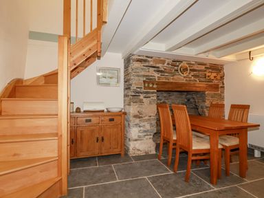 A dining area with wooden table and chairs next to a stone fireplace and wooden staircase at Mill Cottage St Neot