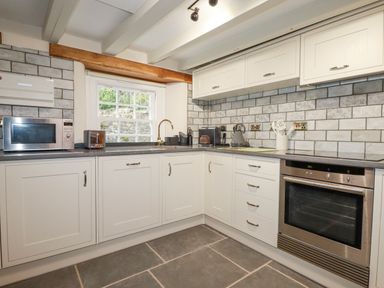 A kitchen with white cabinets a stainless steel oven microwave and various kitchen appliances at Mill Cottage in St Neot
