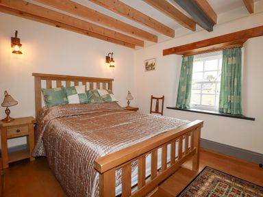 A bedroom with a wooden bed frame bedside tables lamps a window with curtains and exposed ceiling beams at Mill Cottage in St Neot