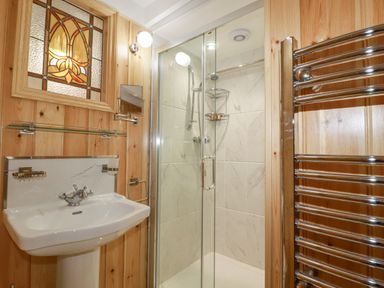 A bathroom with a pedestal sink glass shower enclosure towel warmer and stained glass window at Mill Cottage in St Neot