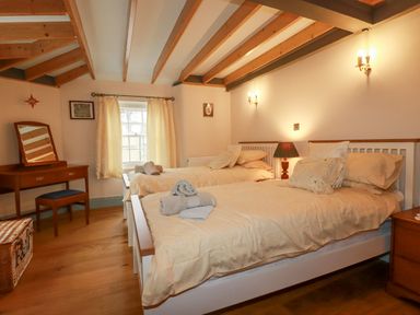A bedroom with two single beds a wooden dressing table and a window at Mill Cottage in St Neot