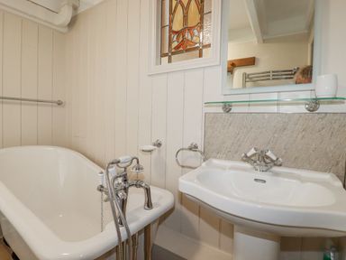 A bathroom with a freestanding bathtub and a pedestal sink with a mirror above at Mill Cottage in St Neot