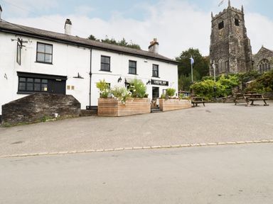 A white building with flower boxes and picnic tables outside near a stone church tower at Mill Cottage in St Neot