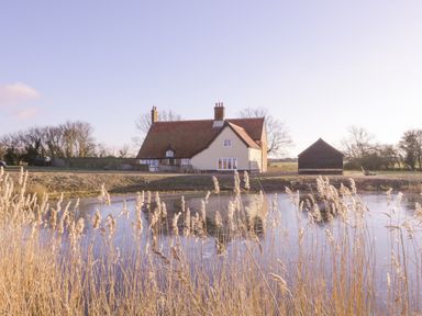 A house with a tiled roof and chimney near a pond with reeds at West House Farm in Leiston