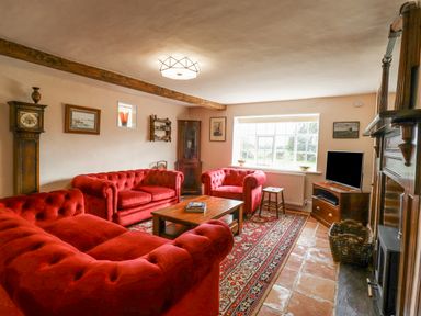 A living room with red sofas wooden coffee table grandfather clock and television at West House Farm in Leiston