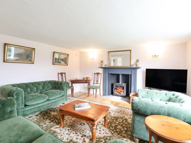 A living room with green sofas a wooden coffee table a fireplace and a television at West House Farm in Leiston