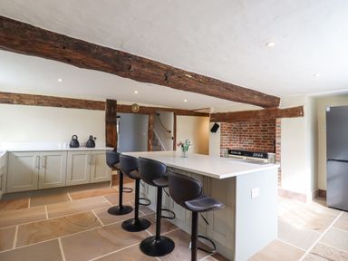 A kitchen with a large island and four black bar stools exposed wooden beams and a brick fireplace at West House Farm in Leiston