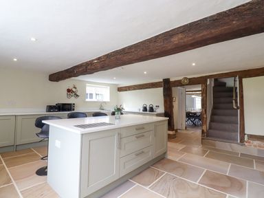 A kitchen with an island and bar stools wooden beams and a staircase at West House Farm in Leiston