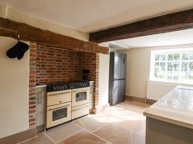 A kitchen with a cream oven in a brick alcove a black refrigerator under wooden beams and a window at West House Farm in Leiston