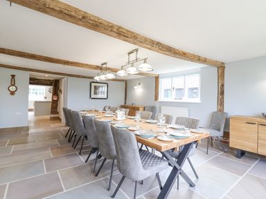 A dining room with a long wooden table set for a meal and gray upholstered chairs at West House Farm Leiston