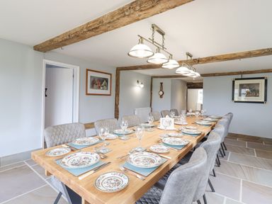 A dining room with a long wooden table set with plates glasses and cutlery and gray upholstered chairs at West House Farm in Leiston