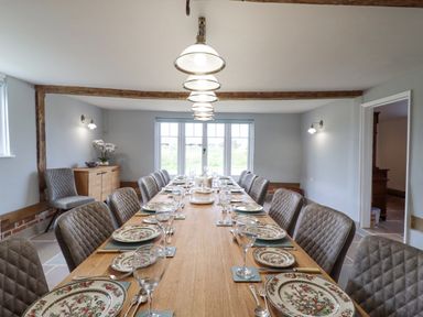 A dining room with a long table set with plates and glassware and padded chairs at West House Farm in Leiston