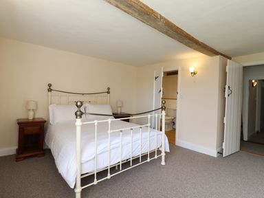 A bedroom with a metal bed frame two bedside tables with lamps an open door to a bathroom and an open door to a hallway at West House Farm in Leiston