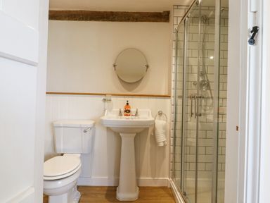 A bathroom with a toilet pedestal sink round mirror and glass shower at West House Farm in Leiston