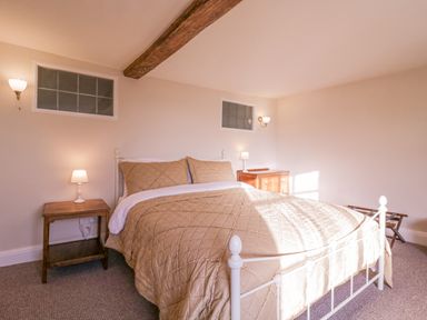A bedroom with a double bed bedside tables lamps wooden chest of drawers and a luggage rack at West House Farm in Leiston