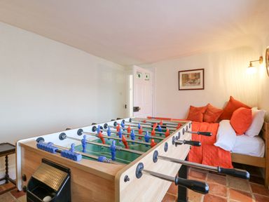 A room with a foosball table and a bed with red bedding and pillows at West House Farm in Leiston