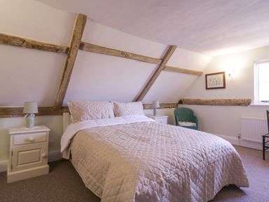 A bedroom with a double bed bedside tables lamps a green armchair a framed picture and exposed wooden beams at West House Farm in Leiston