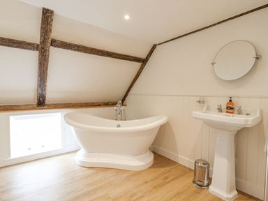 A bathroom with a freestanding bathtub a pedestal sink a round mirror and wooden beams at West House Farm in Leiston