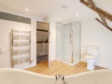 A bathroom with a shower enclosure, toilet, towel radiator, and wooden floor at West House Farm in Leiston