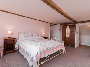 A bedroom with a metal bed frame covered with a quilt and pillows two bedside tables with lamps a wooden wardrobe with a mirror and an open door leading to a bathroom at West House Farm in Leiston