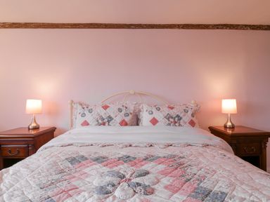 A bed with floral quilt and matching pillows between two wooden bedside tables with lamps at West House Farm in Leiston