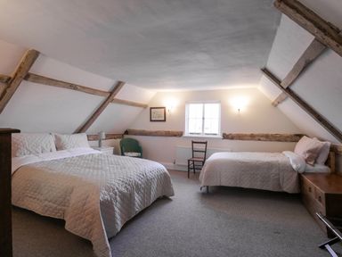 A bedroom with two beds a window and wooden beams on the walls at West House Farm in Leiston