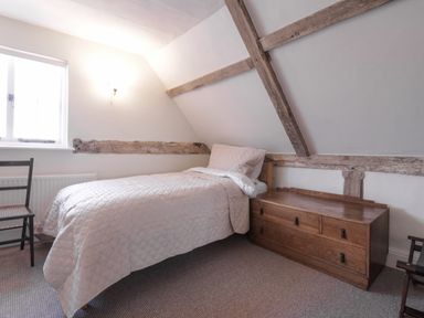 A bedroom with a single bed a wooden chest of drawers and two chairs at West House Farm in Leiston