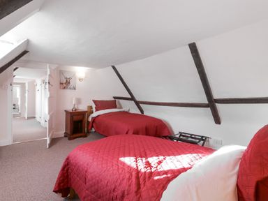 A bedroom with two single beds with red bedding a nightstand with a lamp and exposed wooden beams on the ceiling at West House Farm in Leiston