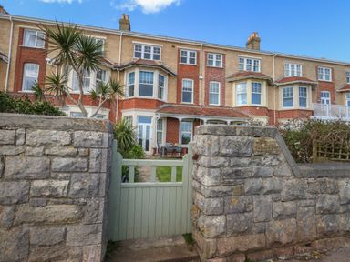 A stone wall with a green wooden gate leading to a garden and a row of brick terraced houses at Blue Yonder in Weymouth