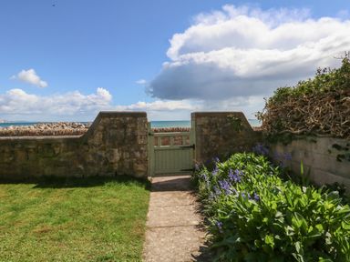 A garden path leading to a wooden gate in a stone wall with the sea and sky in the background at Blue Yonder in Weymouth