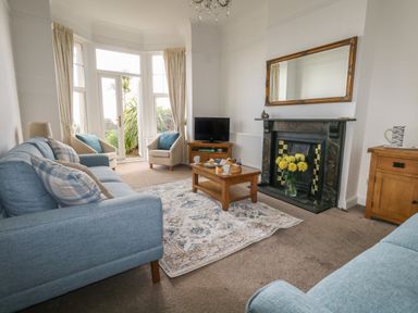 A living room with blue sofas a wooden coffee table two armchairs a fireplace with a mirror above and a TV at Blue Yonder in Weymouth