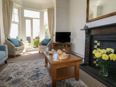 A living room with a wooden coffee table with scones and mugs next to a fireplace and two armchairs near glass doors at Blue Yonder in Weymouth