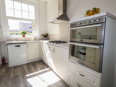 A kitchen with white cabinets a gas stove a double oven a dishwasher and a window with plants at Blue Yonder in Weymouth