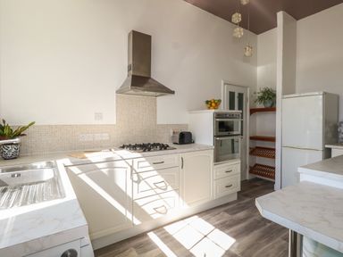 A kitchen with white cabinets a gas stove an oven a refrigerator a sink and shelves with plants and fruit bowl at Blue Yonder in Weymouth