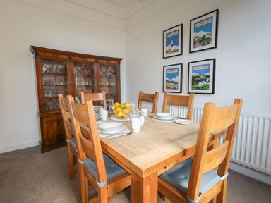 A dining room with a wooden table and six chairs a china cabinet and four framed posters on the wall at Blue Yonder in Weymouth