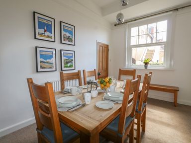A dining room with a wooden table and chairs set with plates and cups a window a door and framed posters on the wall at Blue Yonder in Weymouth