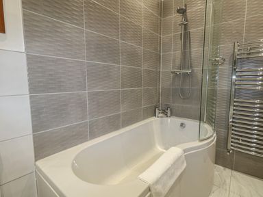 A bathroom with a bathtub shower combination towel on the tub and a chrome towel radiator at Blue Yonder in Weymouth