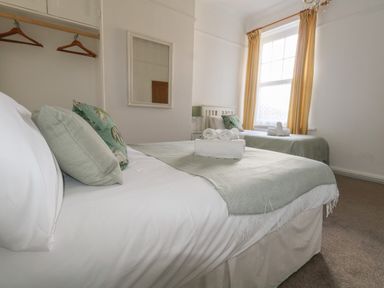A bedroom with two single beds with pillows and folded towels near a window with yellow curtains at Blue Yonder in Weymouth