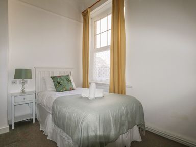 A small bedroom with a single bed a green blanket a floral pillow and a bedside table with a lamp at Blue Yonder in Weymouth