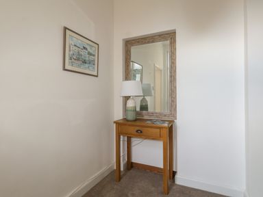 A small wooden table with a lamp and a brochure under a wall mirror and a framed painting on the wall at Blue Yonder in Weymouth