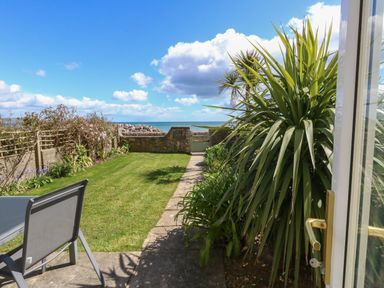 A garden with lawn chairs plants a stone wall and sea view at Blue Yonder in Weymouth