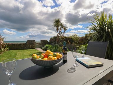 A table with a bowl of fruit wine bottle glasses and a book on a garden patio overlooking the sea at Blue Yonder in Weymouth